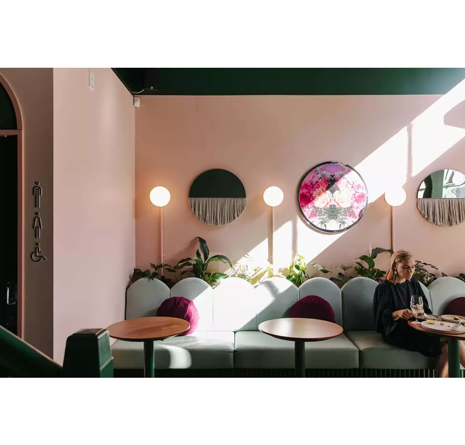 Interior of gin gin, pink wall and mint couches. Lady enjoy a wine at the table.